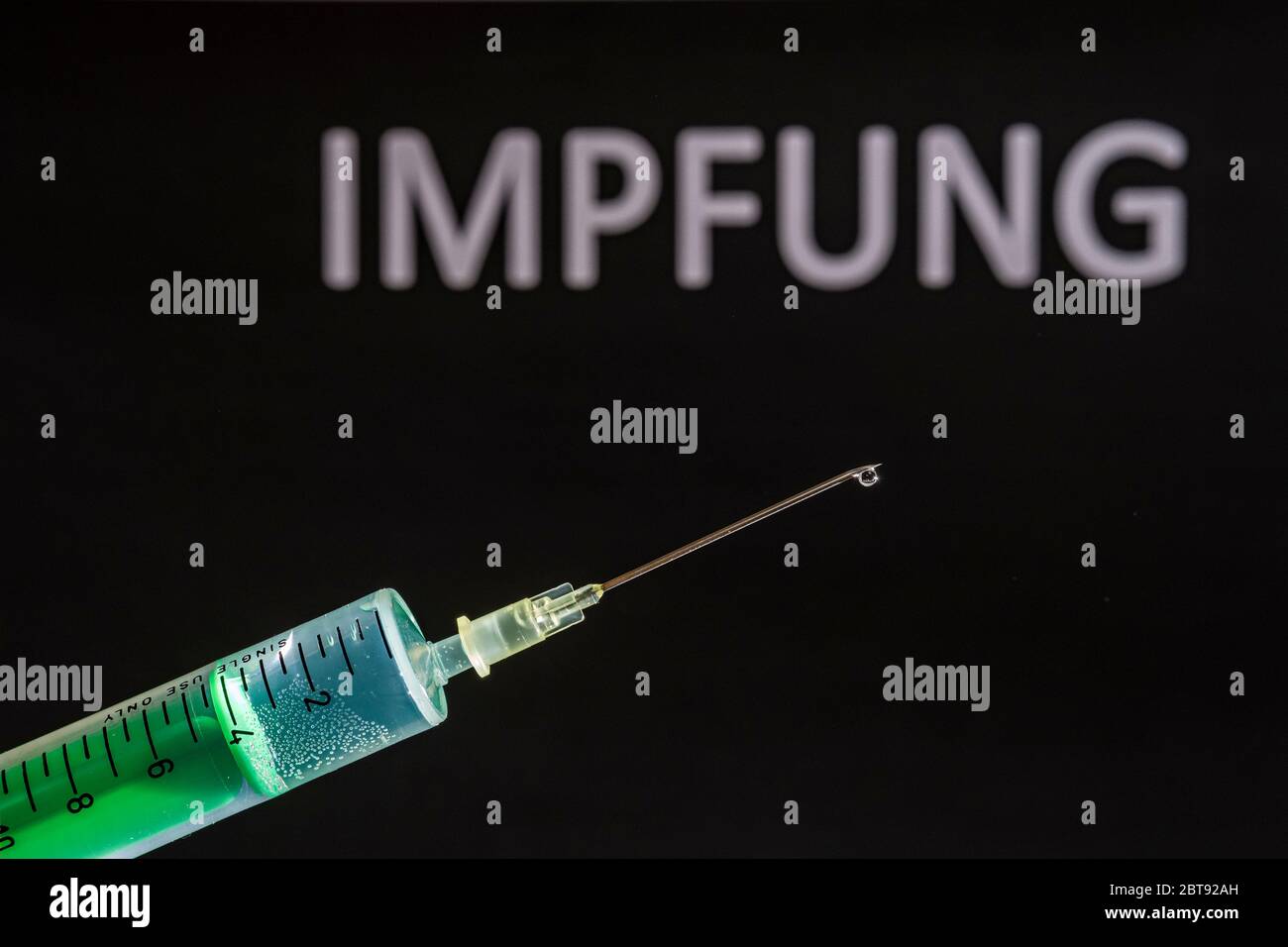 This photo illustration shows a disposable syringe with hypodermic needle, IMPFUNG written on a black board behind Stock Photo