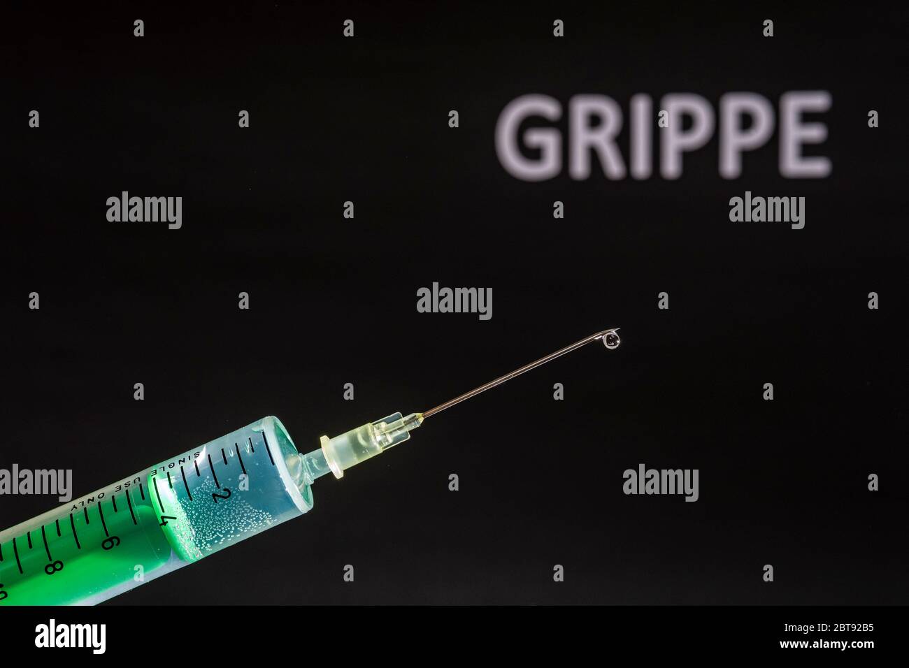 This photo illustration shows a disposable syringe with hypodermic needle, GRIPPE written on a black board behind Stock Photo