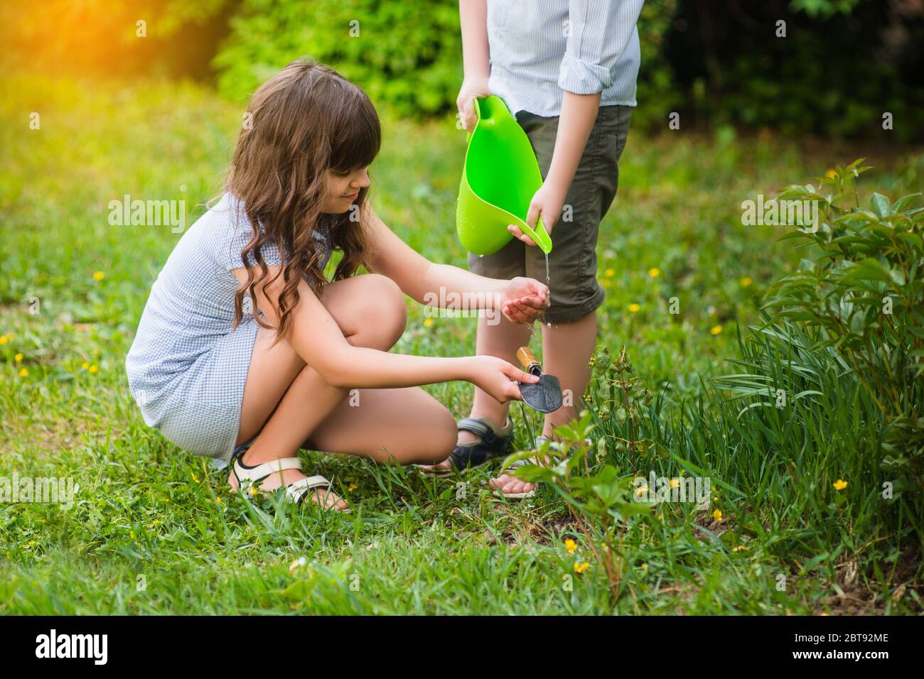 Smiling cute girl and blond boy cleaning horticultura tools in garden on sunny day. Summer activities Stock Photo