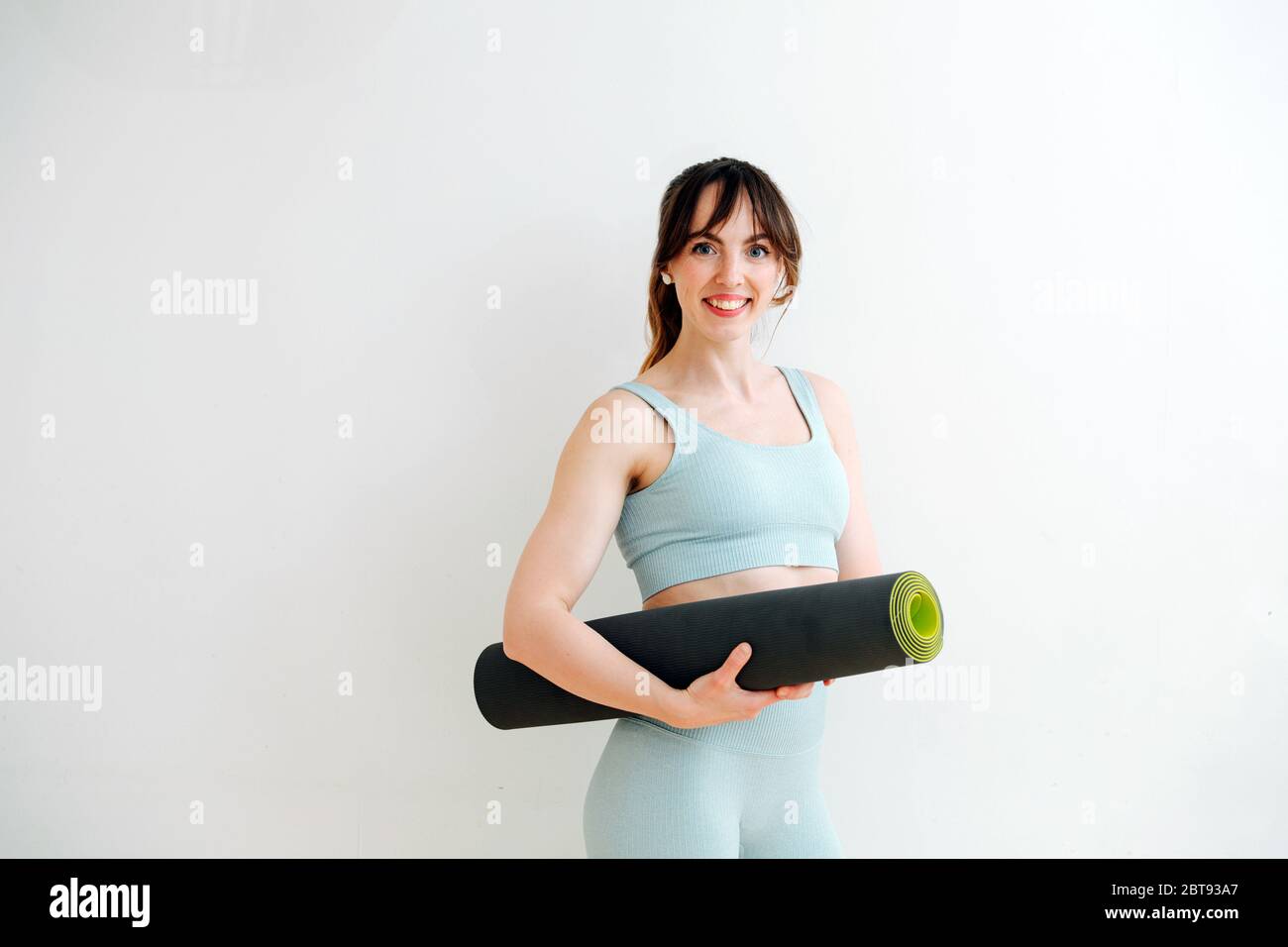 Getting ready for workout. Skinny girl in a sweatsuit holding a rolled-up mat Stock Photo