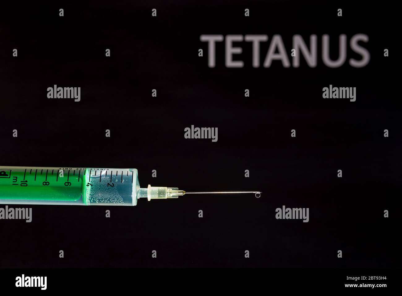 This photo illustration shows a disposable syringe with hypodermic needle, TETANUS written on a black board behind Stock Photo