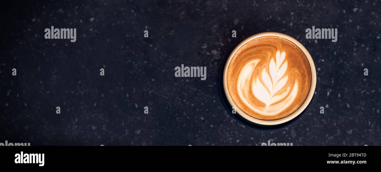 Top view hot capucino coffee cup with latte art foam on black stone table at cafe.dark scene.banner space mock up for adding text Stock Photo
