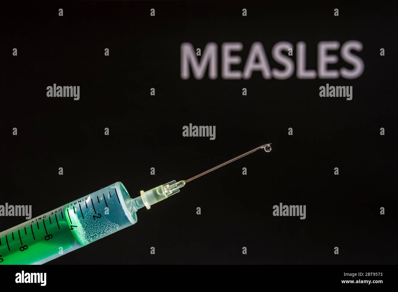 This photo illustration shows a disposable syringe with hypodermic needle, MEASLES written on a black board behind Stock Photo