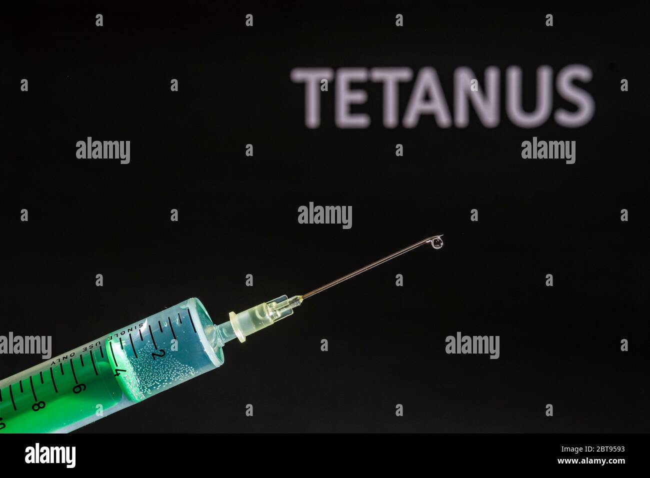 This photo illustration shows a disposable syringe with hypodermic needle, TETANUS written on a black board behind Stock Photo