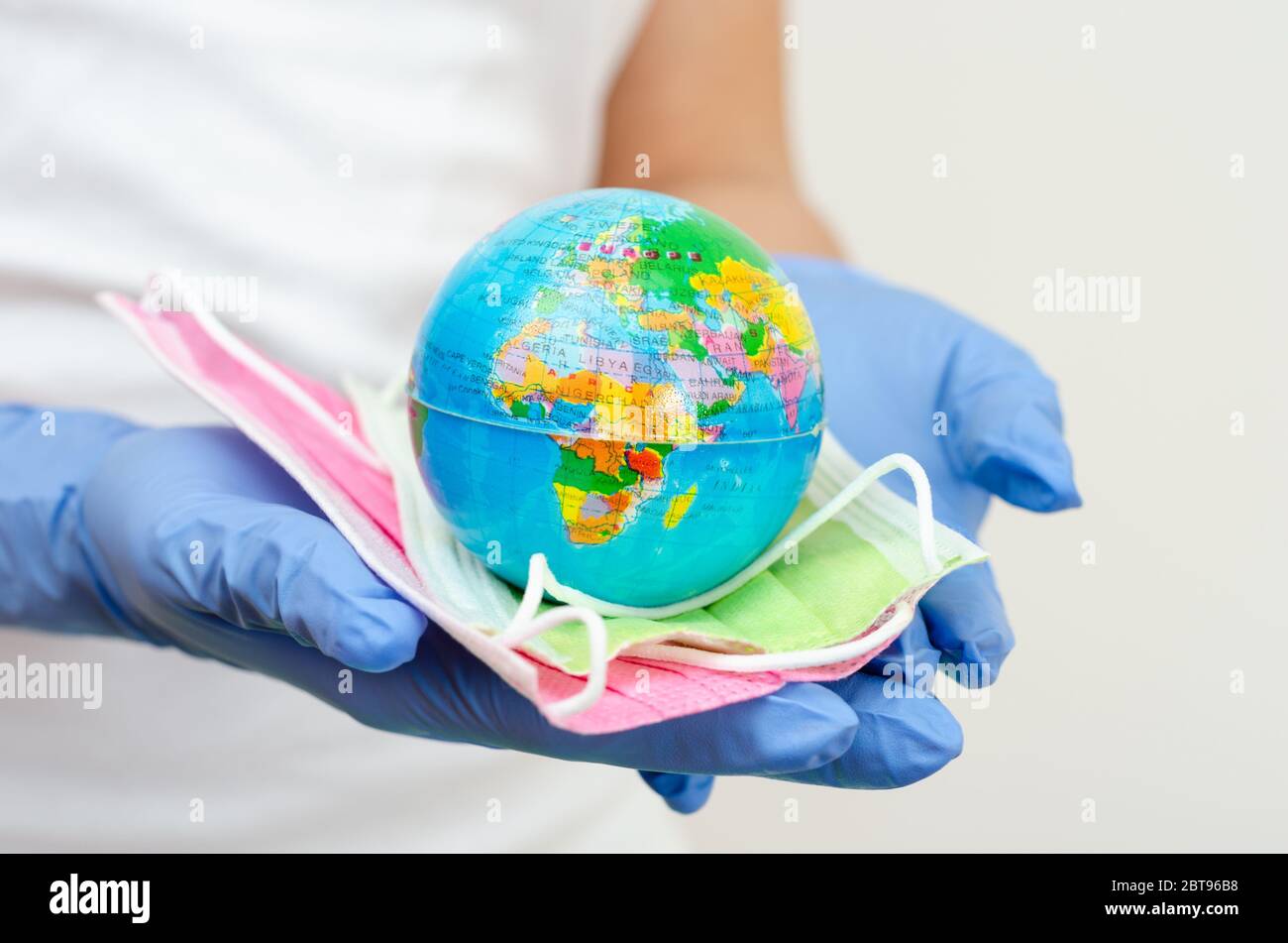 Hands covered with surgical gloves holding earth globe and face masks representing the concept of protecting population against disease transmission Stock Photo