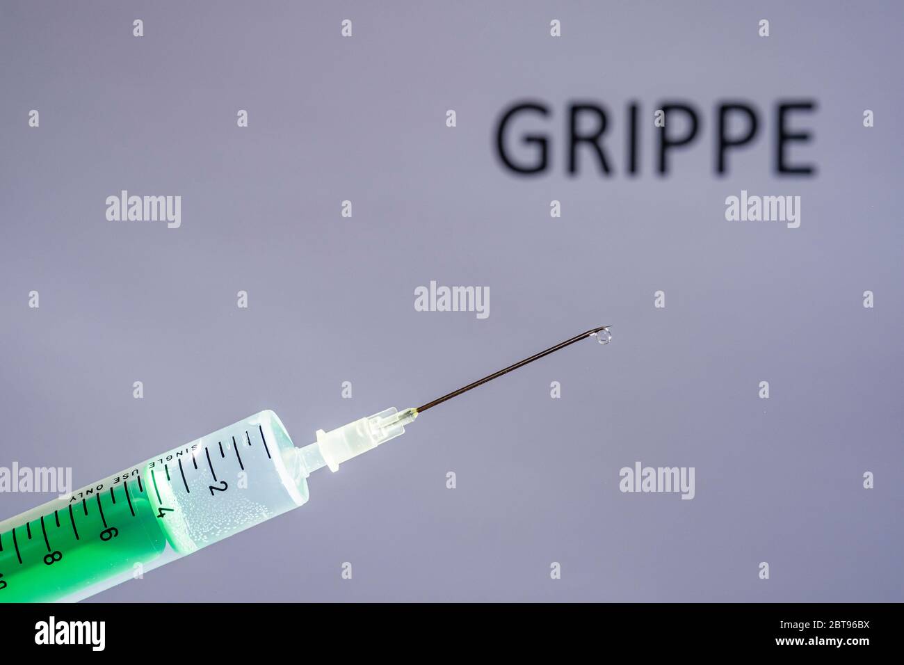 This photo illustration shows a disposable syringe with hypodermic needle, GRIPPE written on a grey board behind Stock Photo