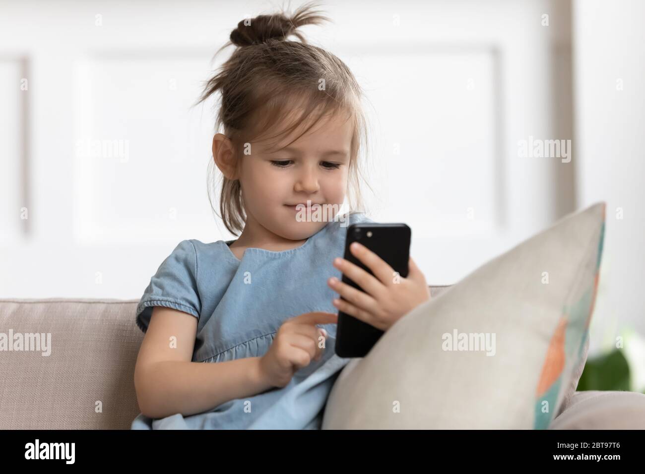 Close up cute little girl holding phone, looking at screen Stock Photo