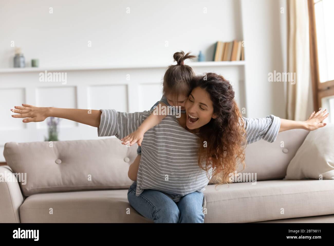 Laughing mother piggybacking little daughter, playing funny game Stock Photo