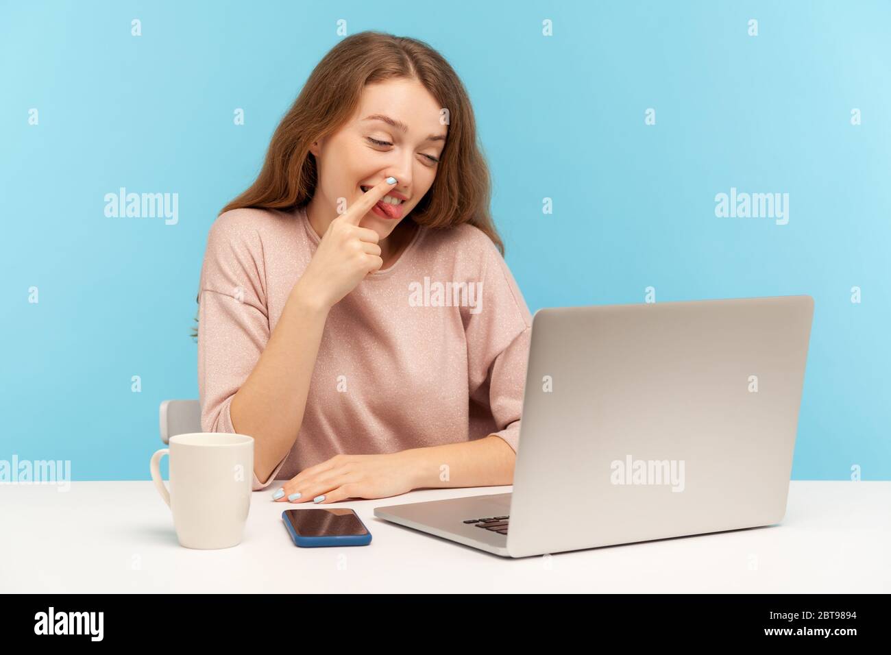 Lazy woman employee picking nose and looking into laptop screen with careless expression, talking on video call on laptop and expressing indifference Stock Photo