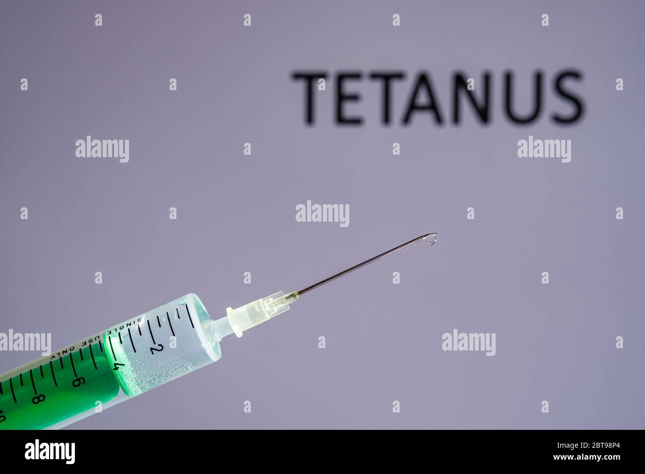 This photo illustration shows a disposable syringe with hypodermic needle, TETANUS written on a grey board behind Stock Photo