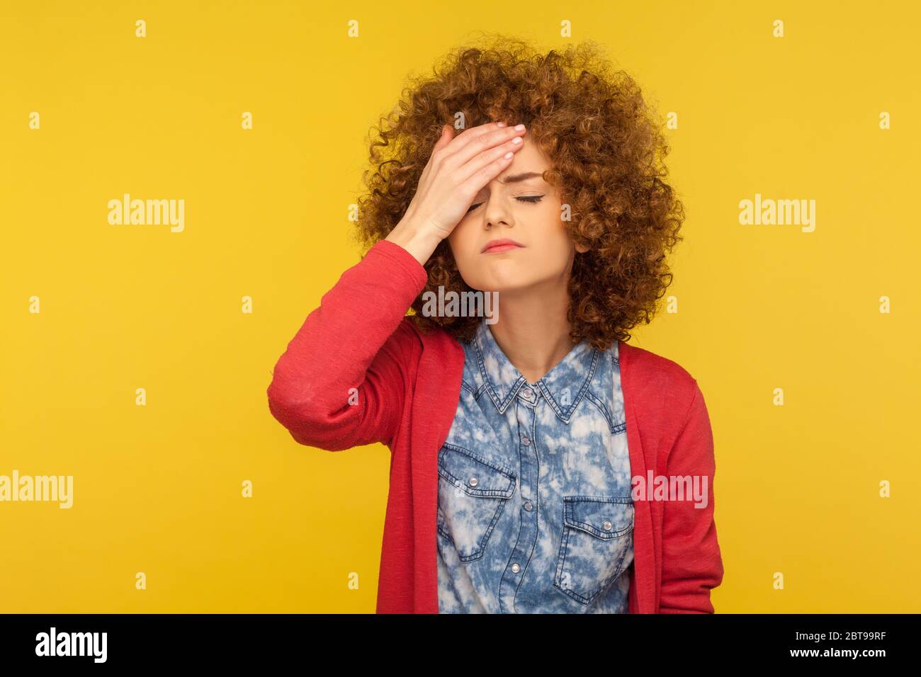 Facepalm. Portrait of depressed woman with curly hair slapping forehead in regret gesture, blaming herself, feeling shame and sorrow, body language. i Stock Photo