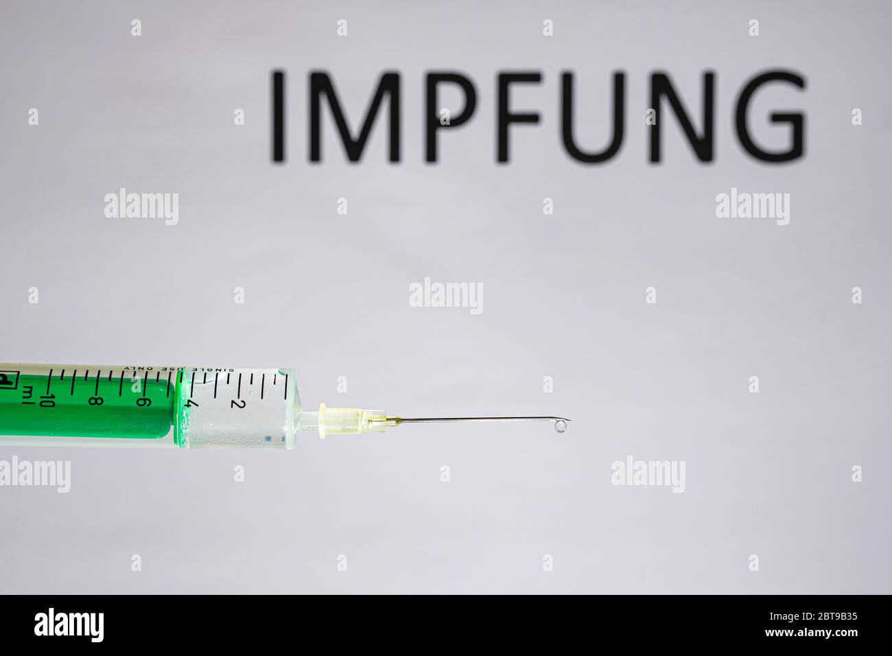 This photo illustration shows a disposable syringe with hypodermic needle, IMPFUNG written on a white board behind Stock Photo