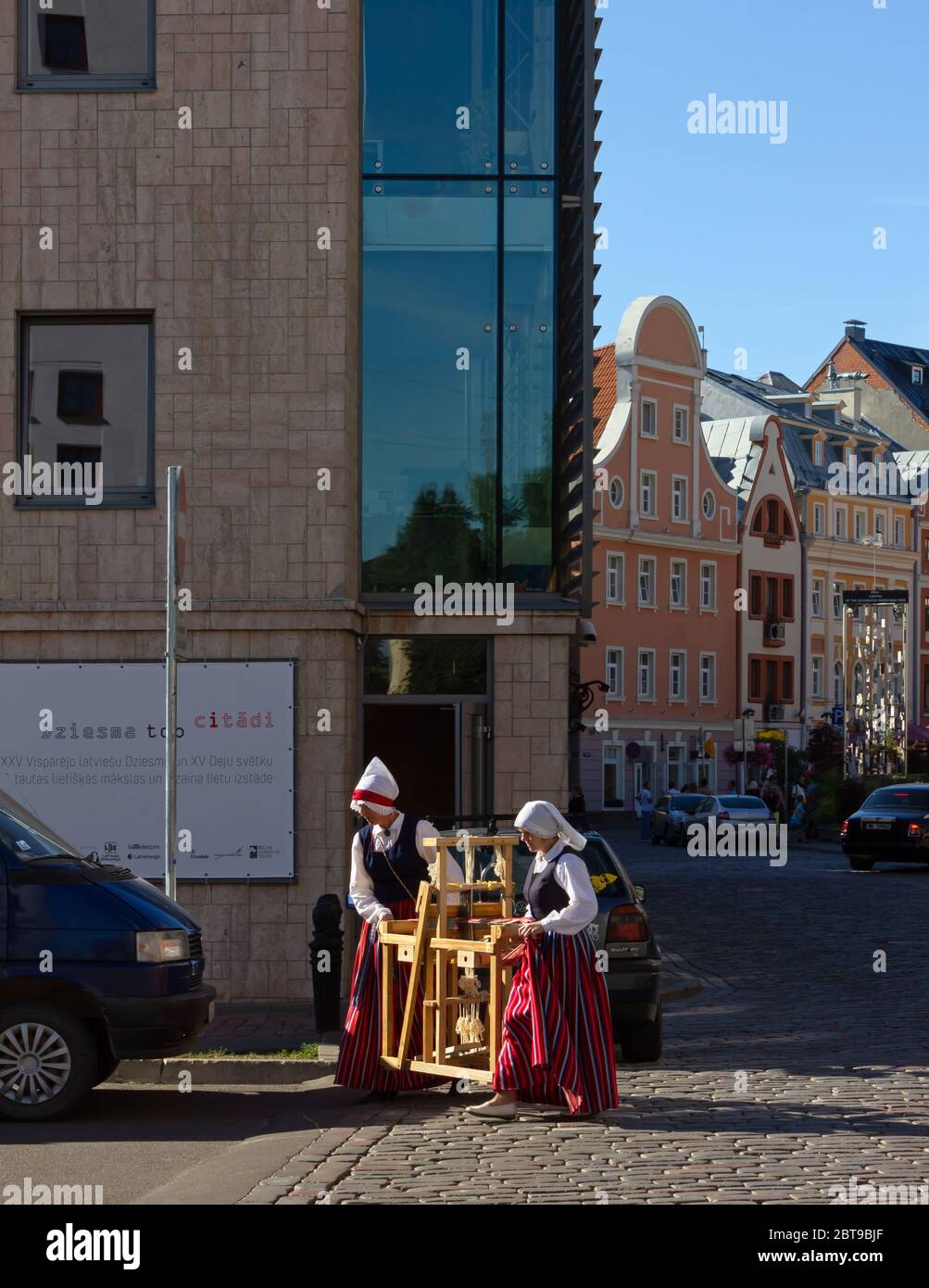 RIGA, Latvia - July 17, 2013: Two women wearing a folk costume are carrying a tradirional wooden artifact on a street in downtown Riga Stock Photo