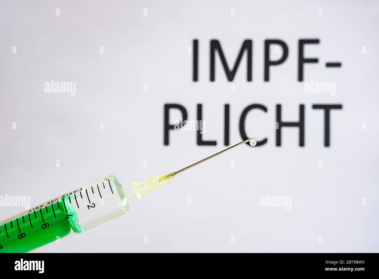 This photo illustration shows a disposable syringe with hypodermic needle, IMPFPLICHT written on a white board behind Stock Photo