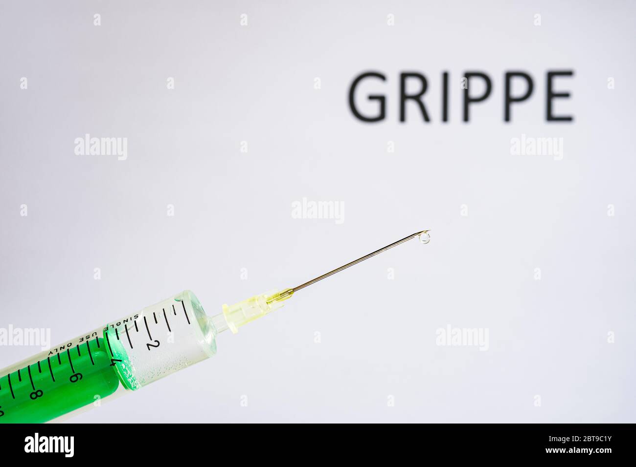 This photo illustration shows a disposable syringe with hypodermic needle, GRIPPE written on a white board behind Stock Photo