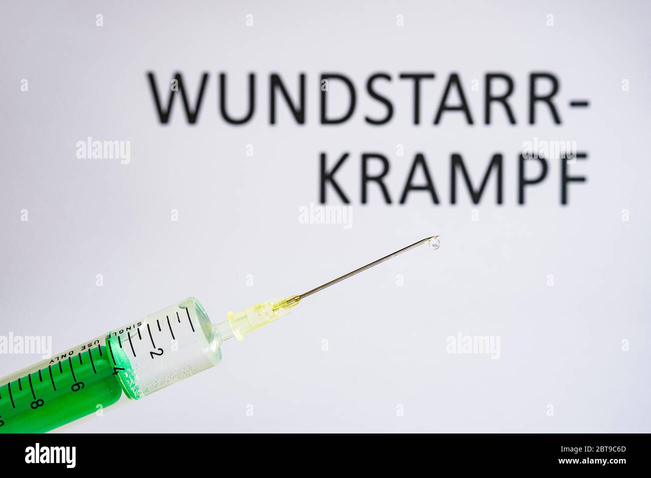 This photo illustration shows a disposable syringe with hypodermic needle, WUNDSTARRKRAMPF written on a white board behind Stock Photo