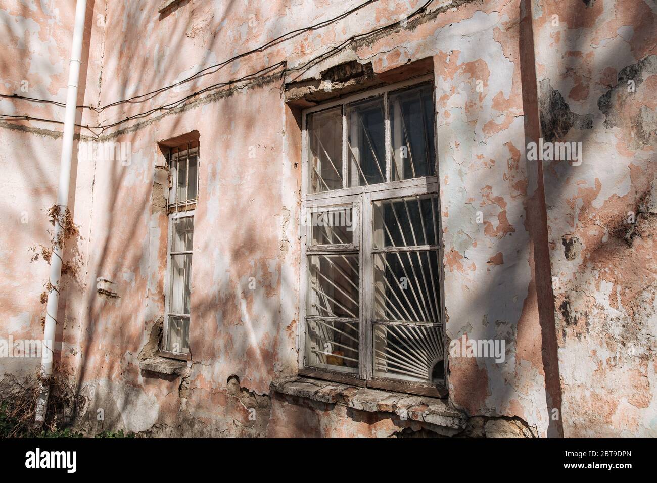 An old, crumbling window with a rusty bars on it. Damaged building. Stock Photo
