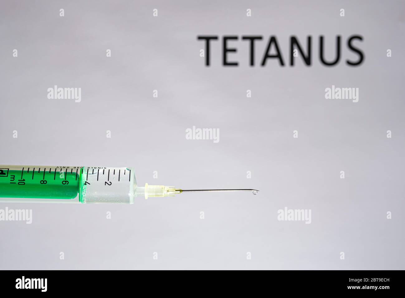 This photo illustration shows a disposable syringe with hypodermic needle, TETANUS written on a white board behind Stock Photo