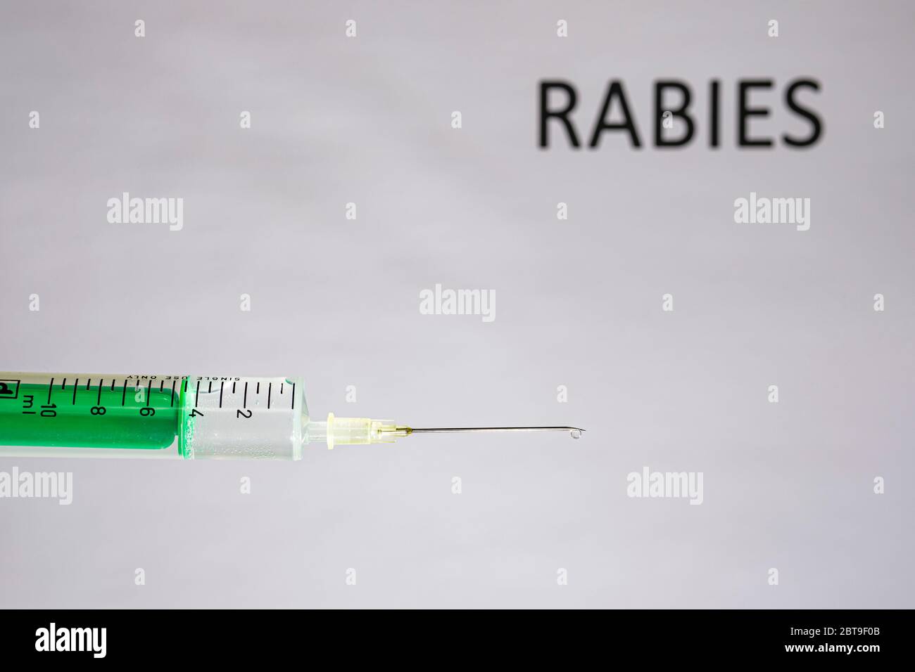 This photo illustration shows a disposable syringe with hypodermic needle, RABIES written on a white board behind Stock Photo