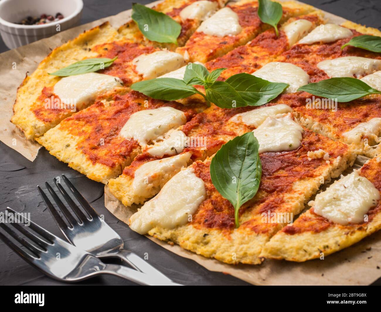 sliced homemade cauliflower pizza crust with mozarella and fresh basil in dripping pan on black concrete background. Stock Photo