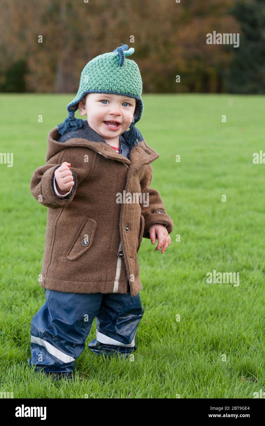 Adorable one year old little boy grinning cheekily and excited to be running about outdoors: Sheffield Park, East Sussex, England, UK. MODEL RELEASED Stock Photo