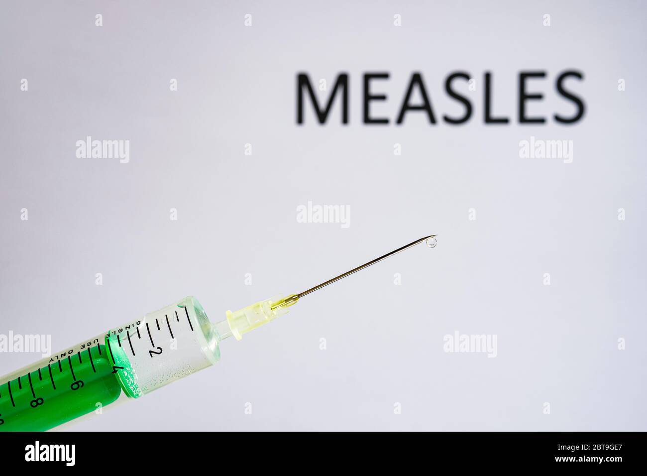 This photo illustration shows a disposable syringe with hypodermic needle, MEASLES written on a white board behind Stock Photo
