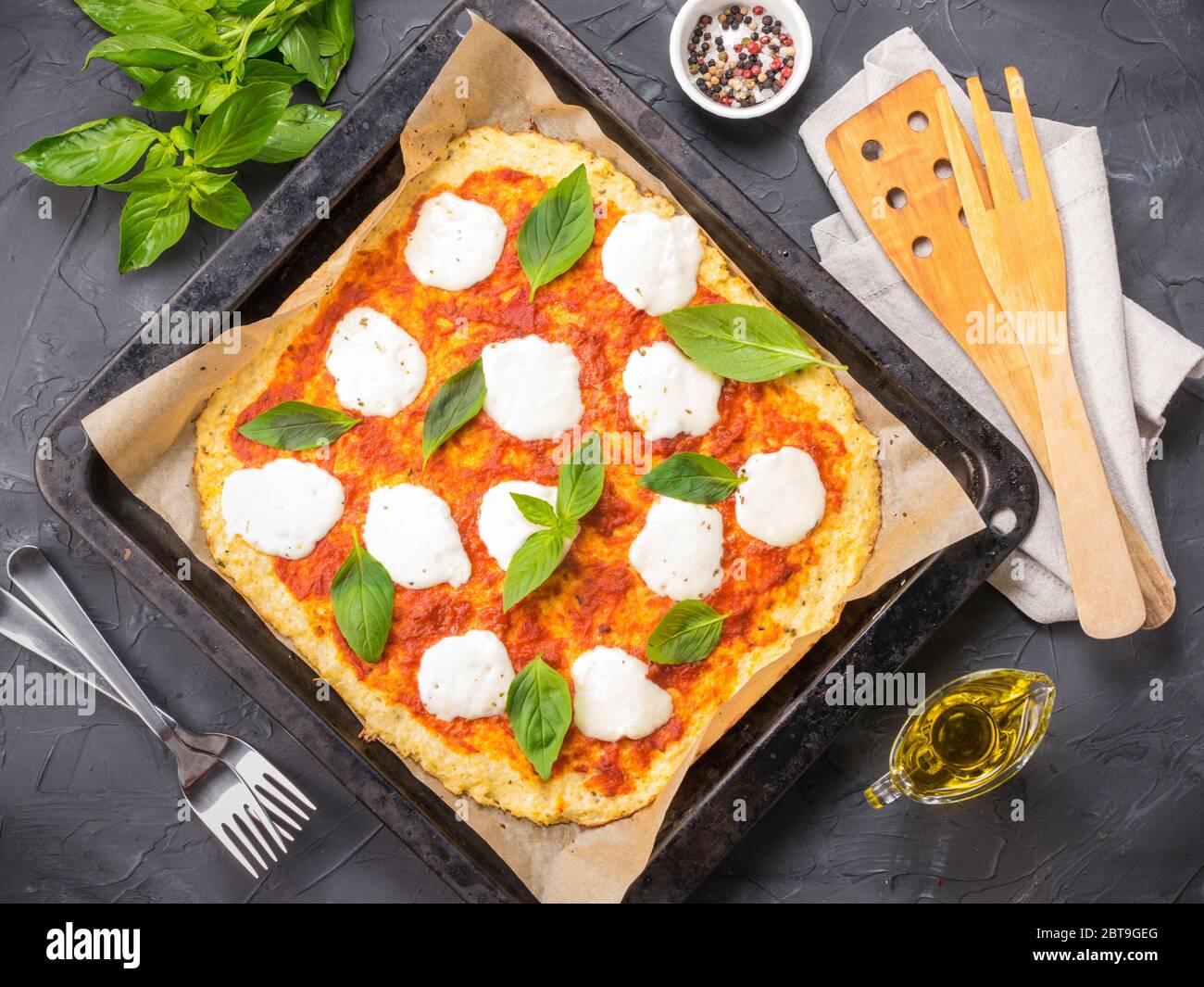 Top view of homemade cauliflower pizza crust with mozarella and fresh basil in dripping pan on black concrete background. Stock Photo