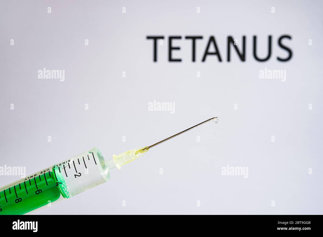 This photo illustration shows a disposable syringe with hypodermic needle, TETANUS written on a white board behind Stock Photo
