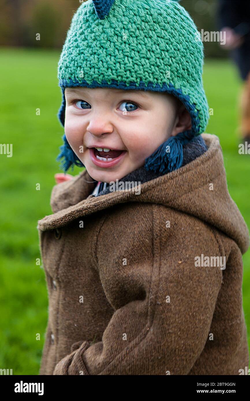 Adorable one year old little boy grinning cheekily and excited to be running about outdoors: Sheffield Park, East Sussex, England, UK. MODEL RELEASED Stock Photo