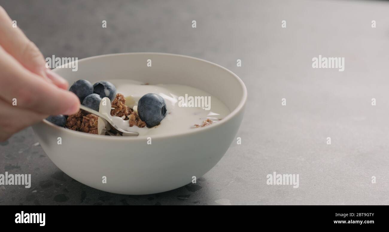 man hand tastes chocolate granola with almond flakes and blueberries in white bowl on concrete surface Stock Photo