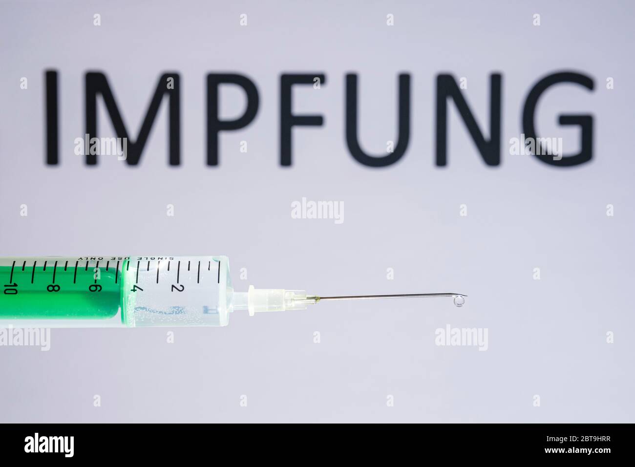 This photo illustration shows a disposable syringe with hypodermic needle, IMPFUNG written on a white board behind Stock Photo