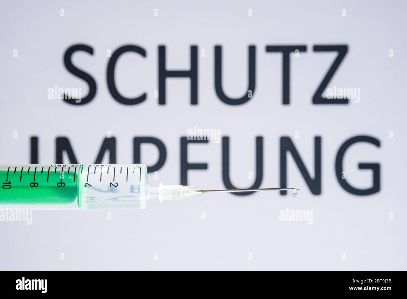 This photo illustration shows a disposable syringe with hypodermic needle, SCHUTZIMPFUNG written on a white board behind Stock Photo