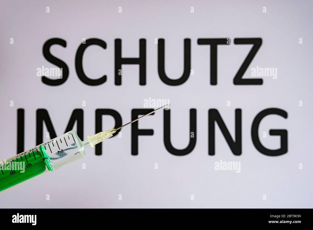 This photo illustration shows a disposable syringe with hypodermic needle, SCHUTZIMPFUNG written on a white board behind Stock Photo
