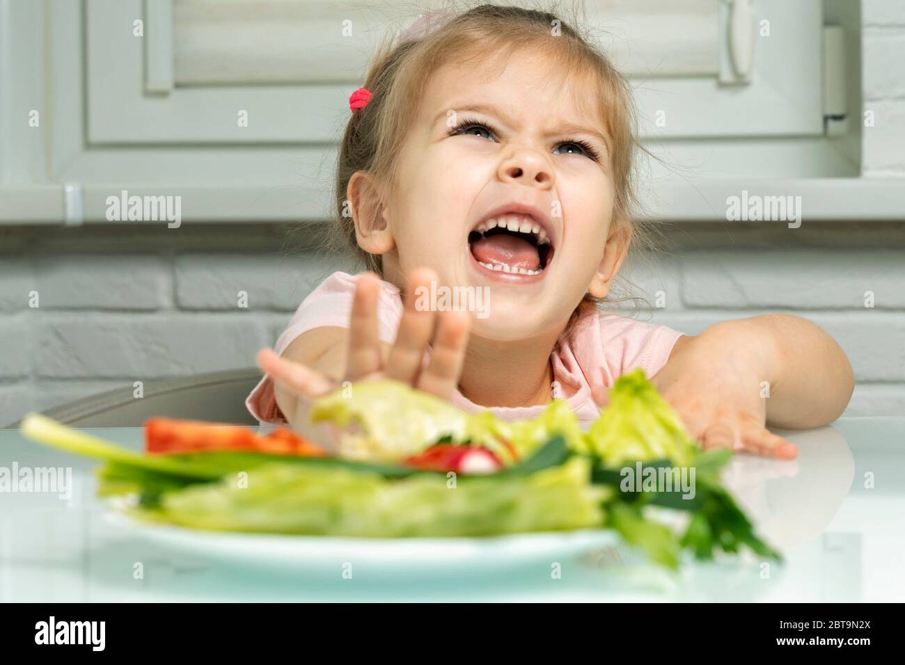 a girl 4 years emotionally repels a plate of vegetables from herself. lack of fruits and vegetables in children's diets Stock Photo