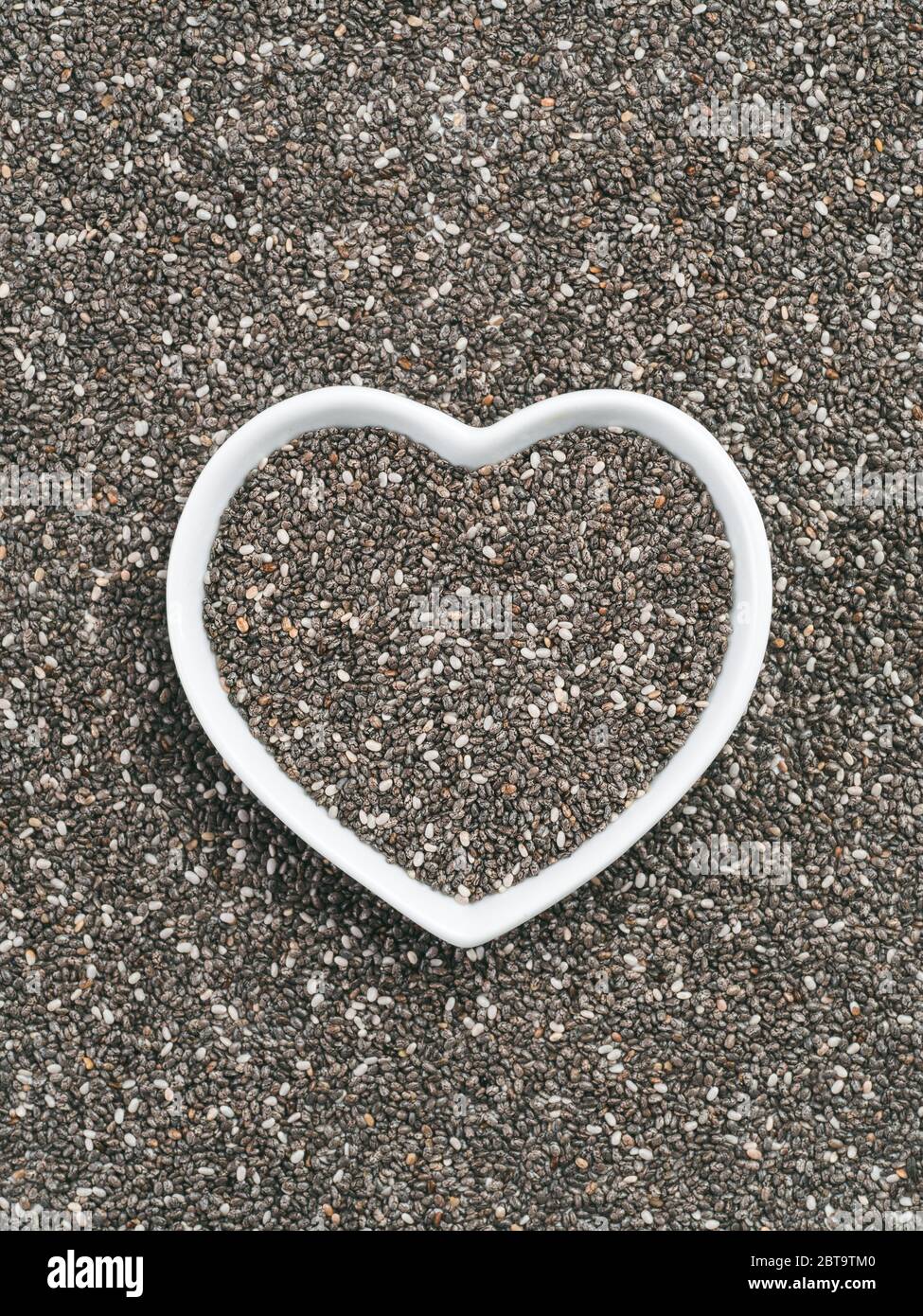 Heart-shaped bowl of chia seeds on chia background. Gluten free and healthy diet. I love chia seeds concept. Copy space. Stock Photo