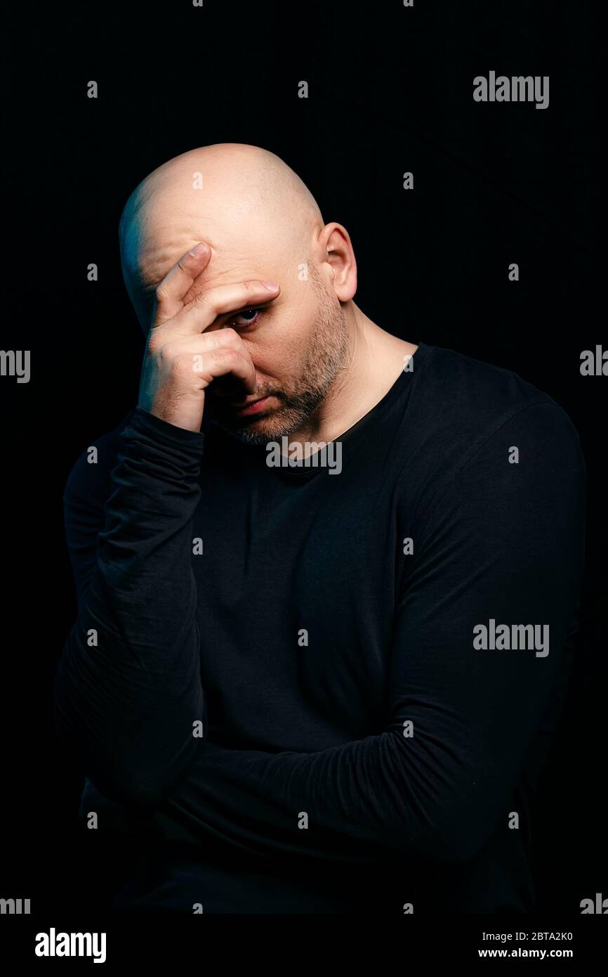 Concerned white bald man with problems in thought on a black background.The problem of alcoholism, impotence or baldness Stock Photo