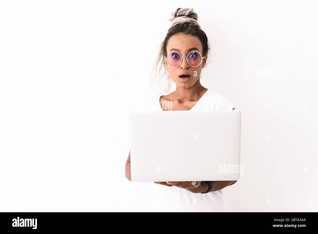 Image of a shocked emotional young african woman with dreads posing isolated over white wall background using laptop computer. Stock Photo