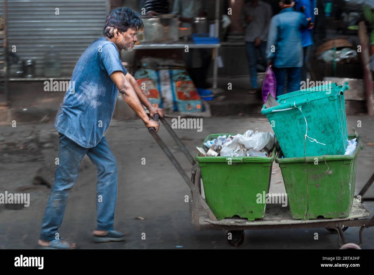 Young Indian pushes an old cart with buckets of rubbish in front of him in a poor area of Mumbay Stock Photo