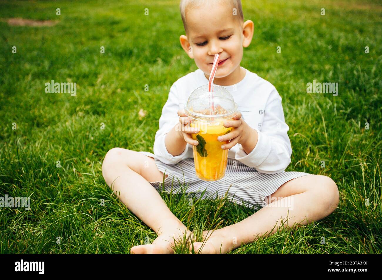 Portrait of happy little boy drinking refreshing orange juice. Smiling child with glass of fresh lemonade Stock Photo