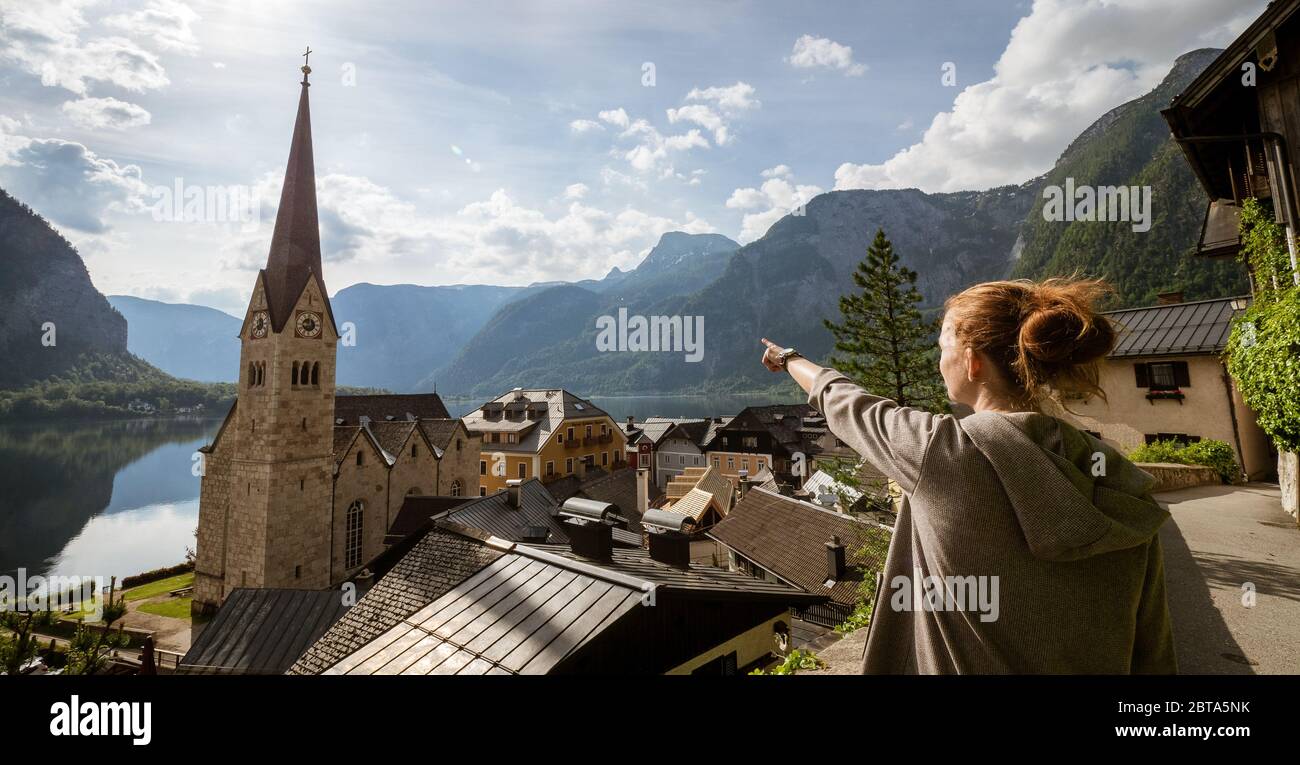 Female tourist pointing at stunning Hallstatt, Salzkammergut region, OÖ, Austria, from an elevated viewing point above the roofs of the famous village Stock Photo
