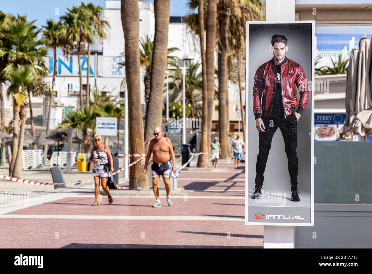 Fashion advertising poster and elderly couple on the promenade at Playa Pinta during phase one of de-escalation of the Covid 19, coronavirus, State of Stock Photo