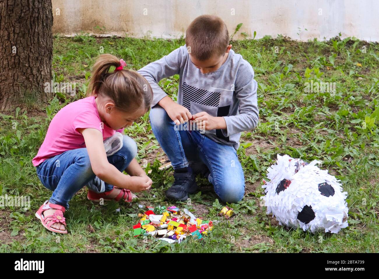 Two kids eat sweets candy on the ground in the garden from a broken