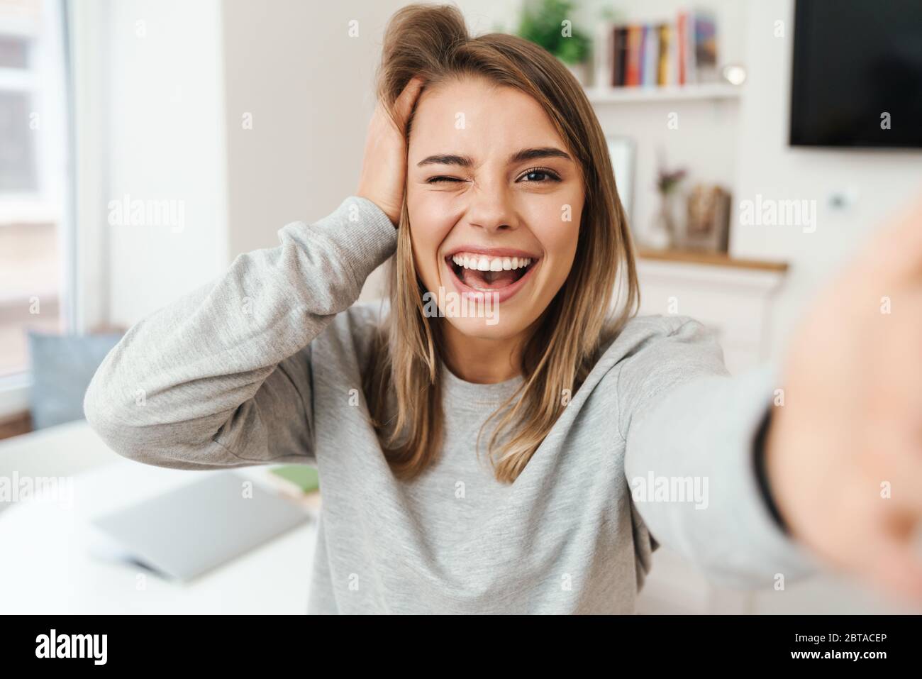 Photo of cheerful young woman laughing and winking while taking selfie ...