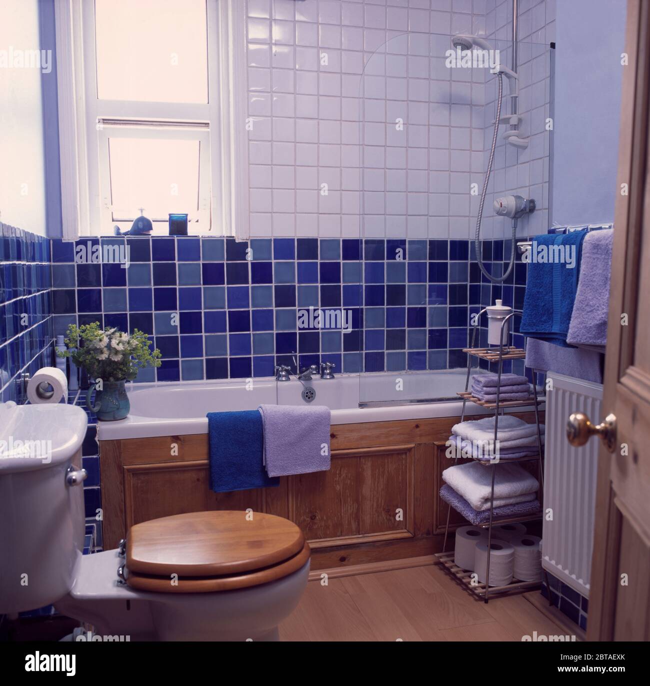 Towels on metal shelves beside bath in blue+white tiled bathroom Stock Photo
