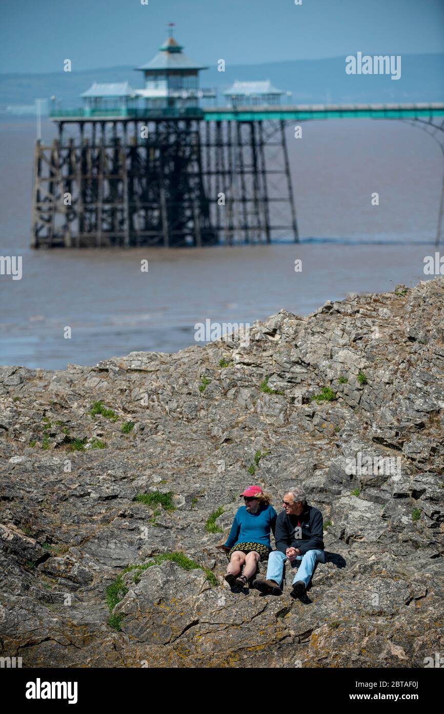 A couple sit on rocks on the beach with the pier in the background at Clevedon, Somerset after coronavirus lockdown restrictions were eased last week. Stock Photo