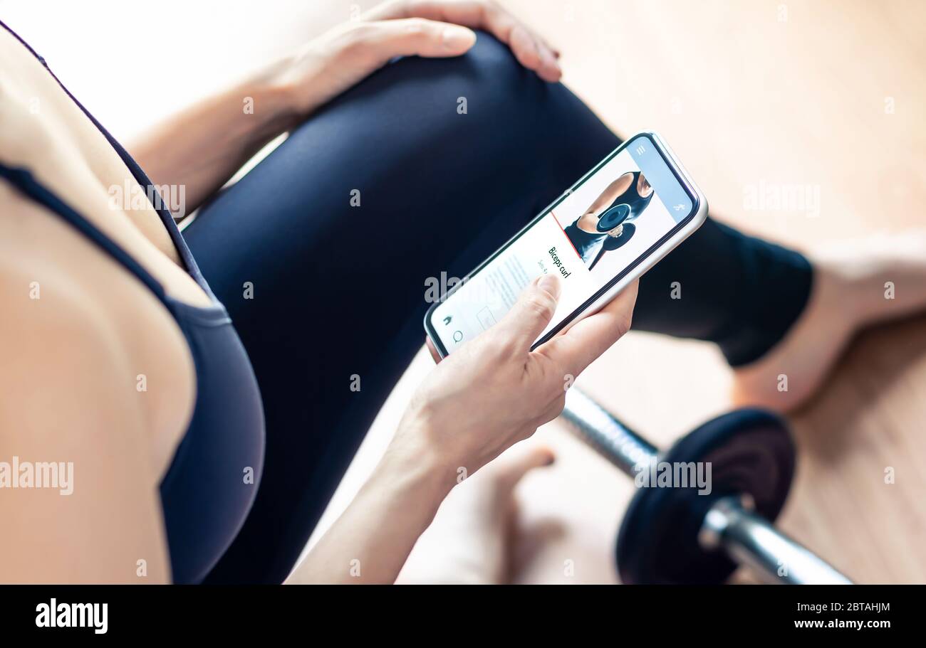 Workout app in mobile phone. Fit woman home training. Gym motivation from online personal trainer. Person watching tutorial video with smartphone. Stock Photo