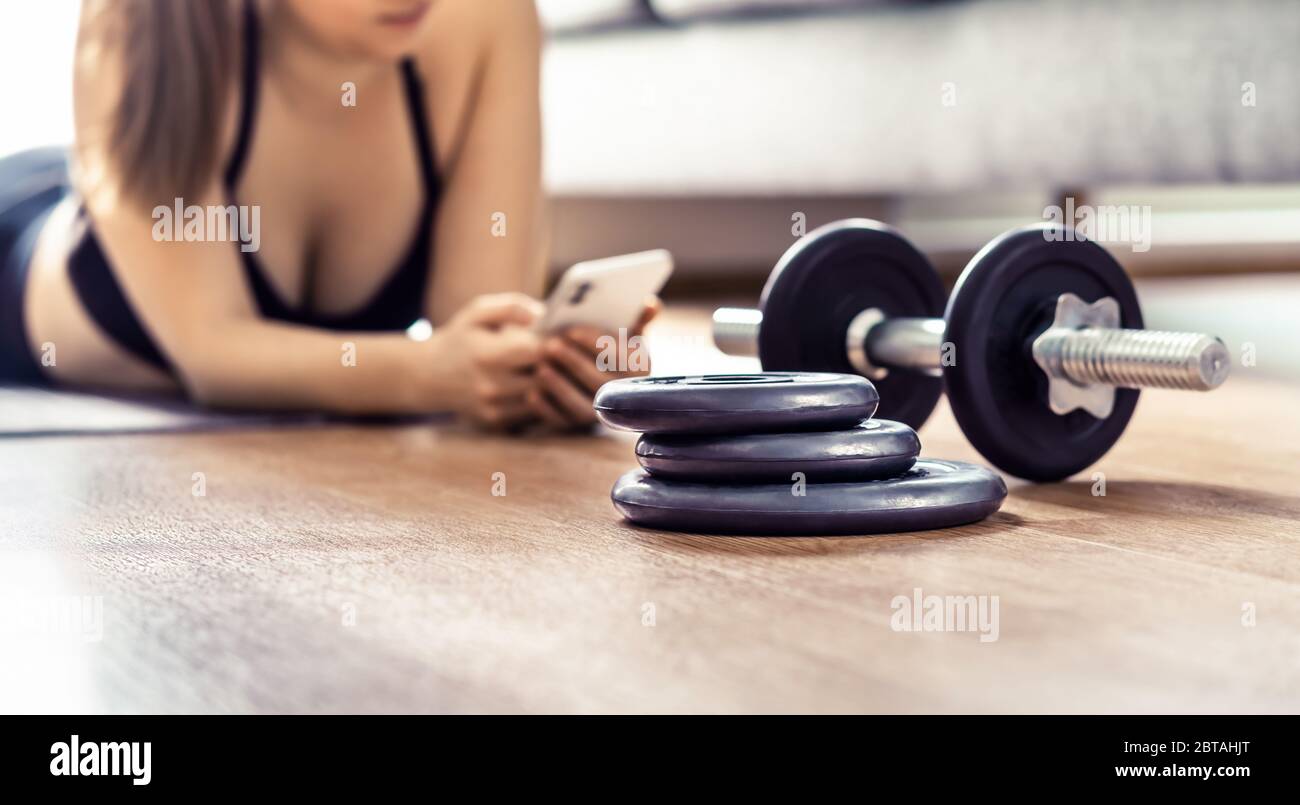 Fit woman using phone during home workout. Online training app or personal trainer course. Exercise routine and program in cellphone. Stock Photo
