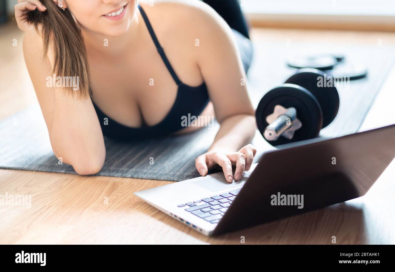 Home exercise and online workout course. Fit woman using laptop during physical training. Pretty girl watching internet class with computer. Stock Photo