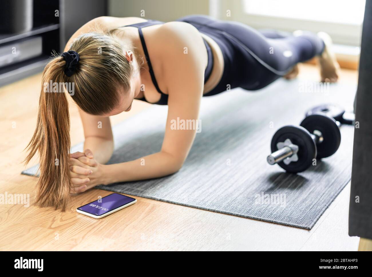 Home exercise and bodyweight training, plank. Fit woman taking time with sport tracker app in phone. Workout routine in living room gym. Stock Photo