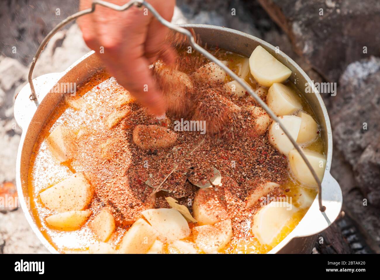 Adding spices in a soup with vegetables. Preparing of a soup on open fire, camping meal. Close-up photo with motion blur effect Stock Photo